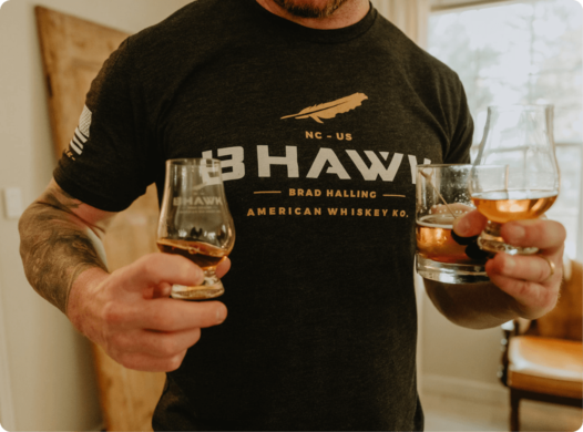 Man wearing BHAWK T-shirt holding BHAWK whiskey glasses